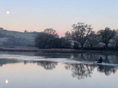 A rower disturbs the glassy surface of the River Dart in winter