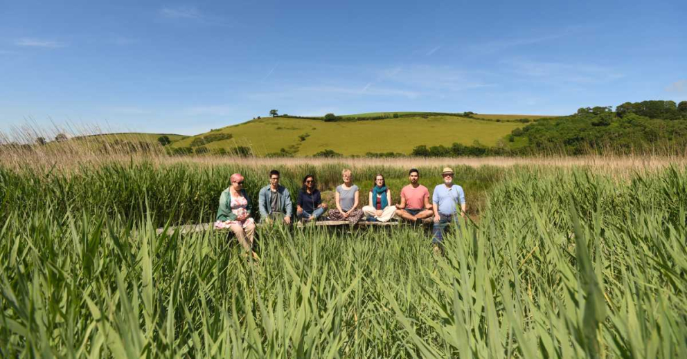 People meditating whilst sat on bench in reed beds at The Sharpham Trust